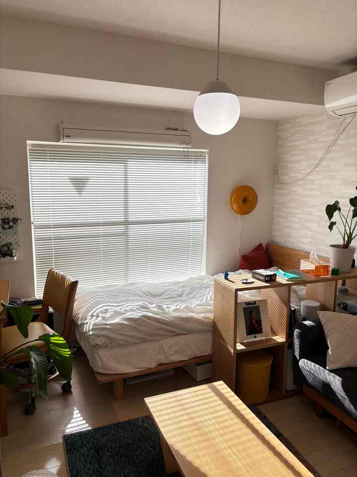 Bright 1K bedroom-living room with white and natural brown tones featuring wooden furniture and a cozy atmosphere