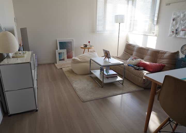 白い壁とベージュのソファ、ビーンバッグが配置された、落ち着いたミニマルな一人暮らしのリビング空間