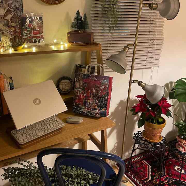 温かみのあるウッドトーンとナチュラルな植物が配置された居心地の良いホームオフィス。ブラインドとフロアランプが照らすコンパクトな空間