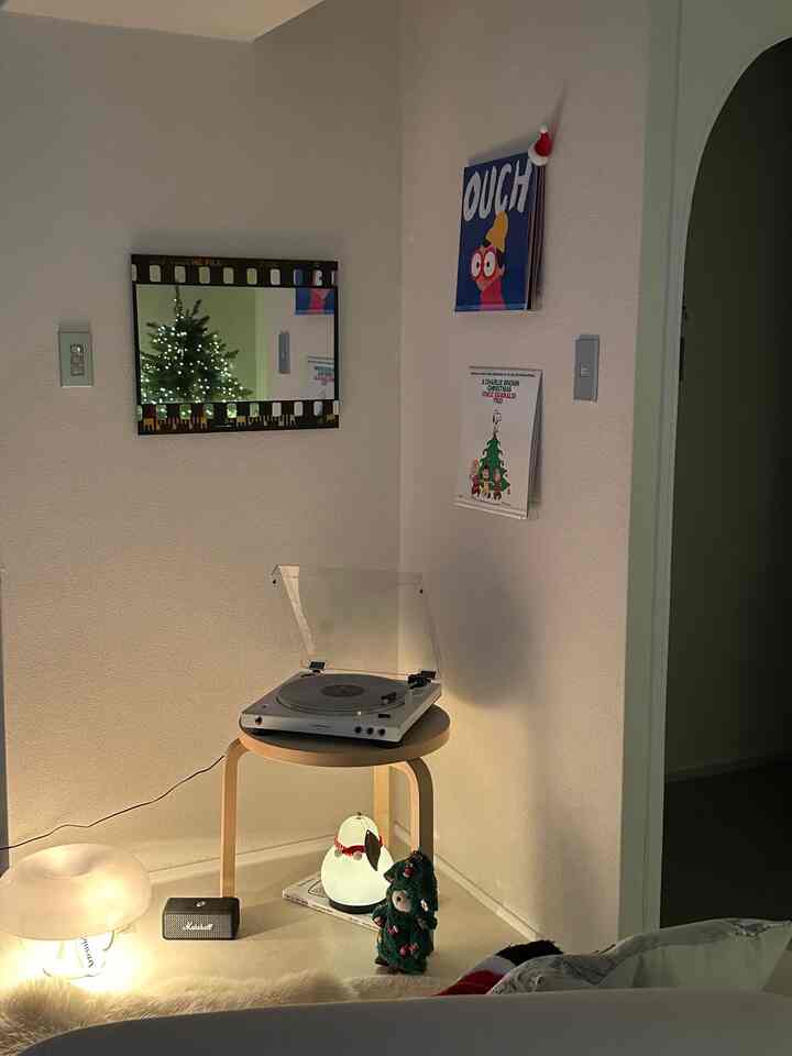 暖かい照明が灯る白を基調としたリビングのコーナーに、レトロなターンテーブルが置かれた木製スツールが配された雰囲気のある空間