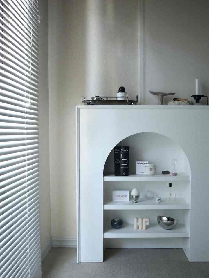 白とモノトーンのリビング、シンプルなマントルピースとオブジェが配置された印象的なミニマルインテリア