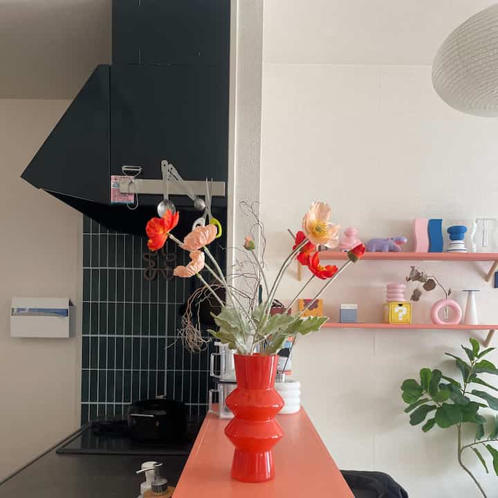 明るく暖かい雰囲気のキッチン、オレンジ色の花瓶と花、ピンクの棚と植物が配置された印象的な空間