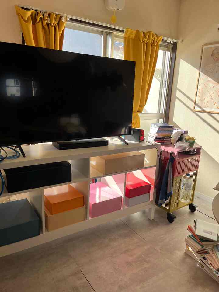 黄色いカーテンとカラフルな収納ボックスが配置された白のテレビ台があるリビングの雰囲気のある空間