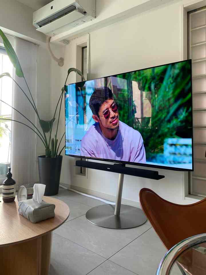 白い壁と黒い家具が調和するミッドセンチュリーモダンなリビング、 大型テレビとレザーバタフライチェアが配置された空間