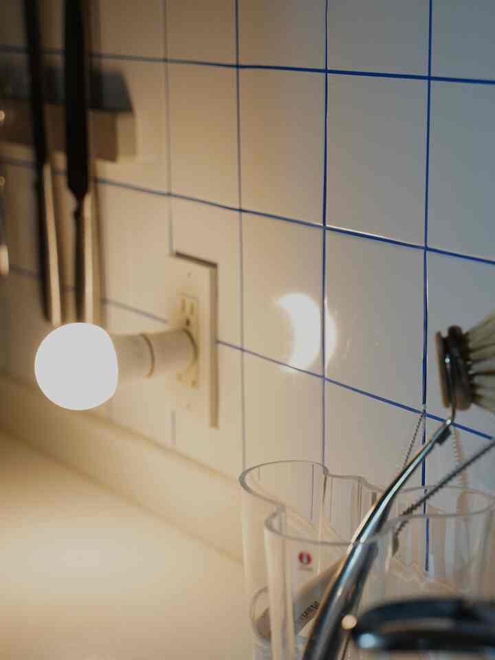 青い目地が映える白いタイルと透明な花瓶が置かれた、照明のあるキッチンの壁面