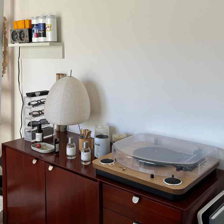ブラウンのキャビネットの上にアイボリーの和紙ランプとアナログプレーヤーが置かれた、すっきりとしたリビング小物のある空間