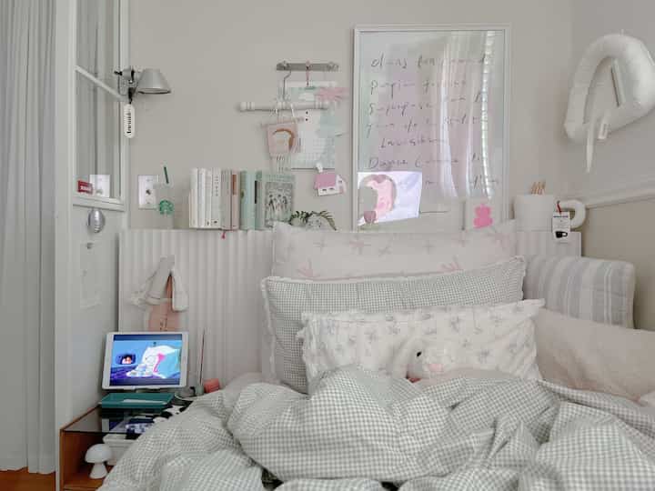 ホワイトとグレーのトーンが特徴の小さな寝室、ベッドと本棚、ナイトテーブルが配置された印象的な空間