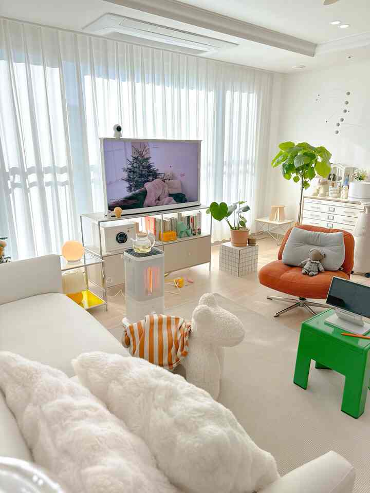 明るいホワイトトーンのリビング、白いソファとオレンジのアームチェア、大きなカーテンとラグが調和した清潔感のある空間