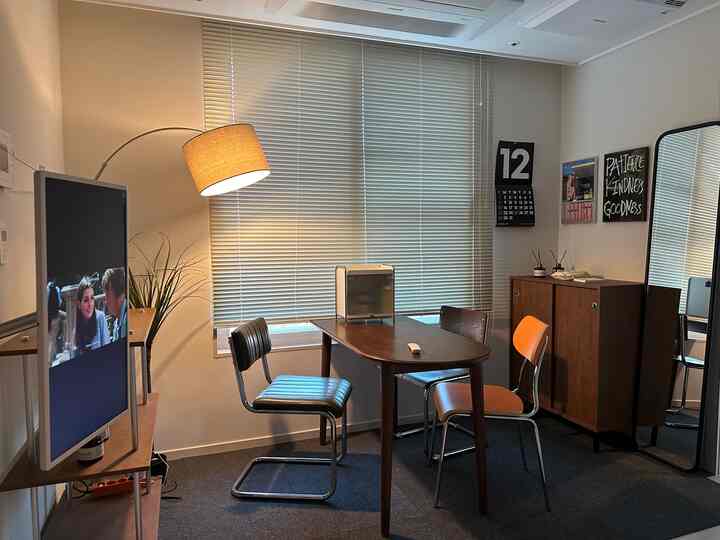 温かみのあるブラウンとホワイトのトーンのミッドセンチュリーモダンなリビング、広い窓とブラインド、中央には木製ダイニングテーブルと椅子が配置された印象的な空間