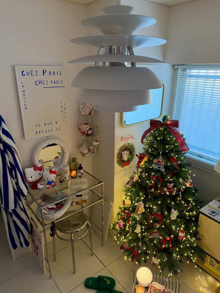 ホワイトとシルバーのトーンの小さなリビングルーム、メタルスツールと化粧台、飾られたクリスマスツリーが温かみのある雰囲気を演出する空間