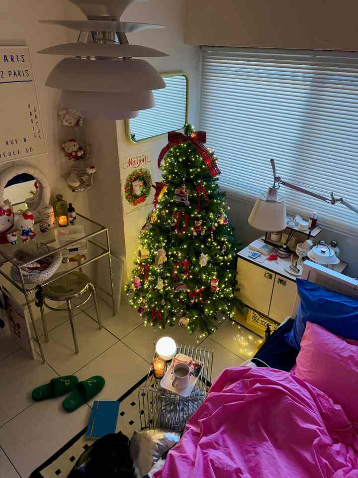 White and pink compact living space featuring a decorated Christmas tree, stainless steel stool, and vanity for a cozy atmosphere