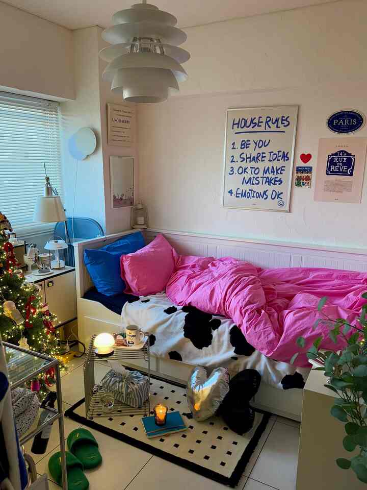 ホワイトとピンクの色調の寝室、ピンクの寝具と青いクッションが置かれたベッドとクリスマスツリーがある雰囲気のあるインテリア