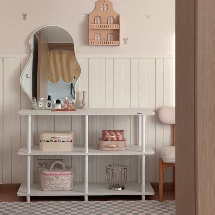 Bright white-toned room featuring a simple shelf with a uniquely shaped mirror and decorative items in a cozy bedroom setting