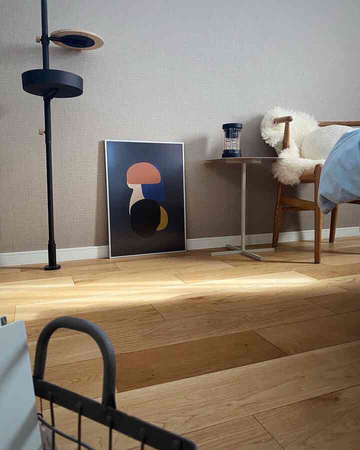 Modern bedroom with wood tone flooring and beige walls, featuring side table and abstract framed poster