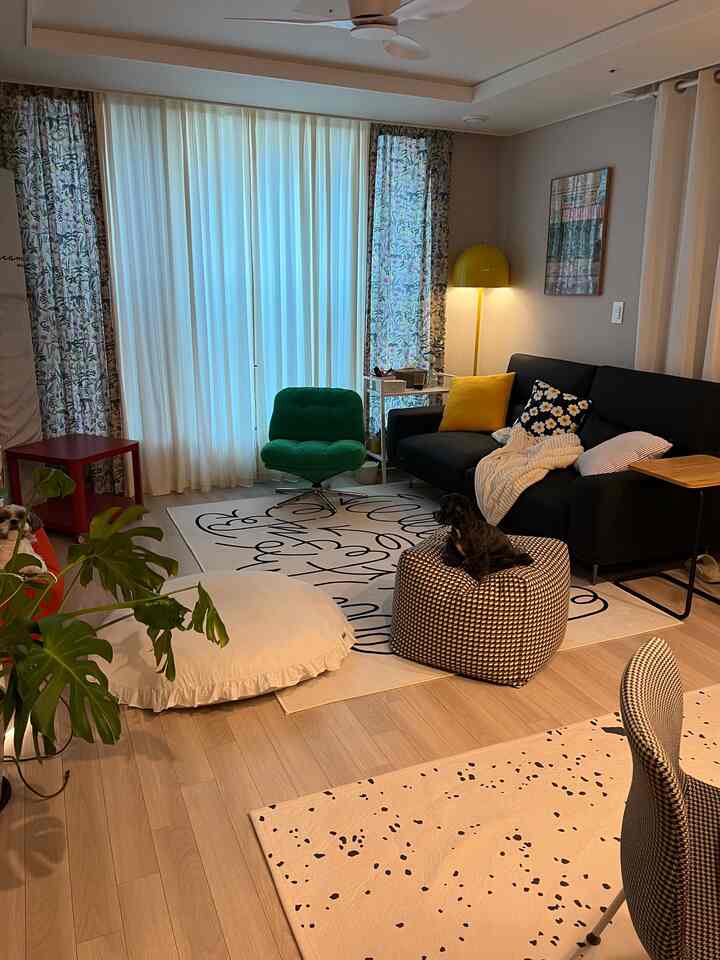 ナチュラルカラーの23坪リビング、黒いソファと緑のアームチェア、ラグの上にペットの犬がいる居心地の良い空間