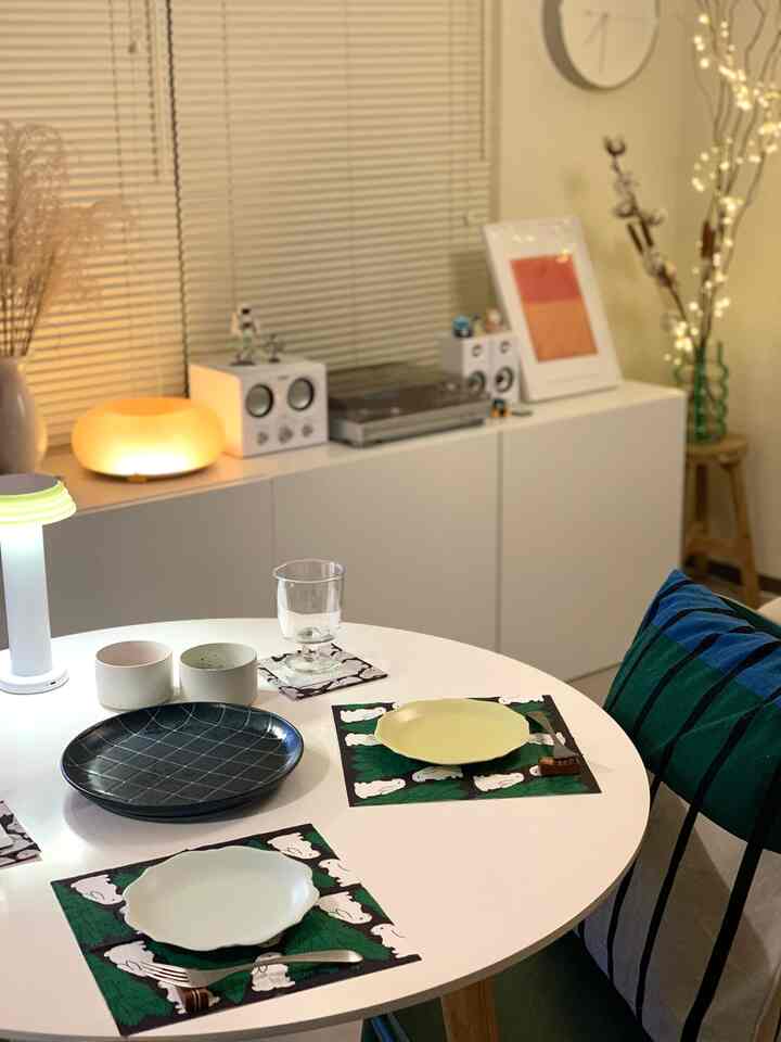 ナチュラルな色調のダイニングルーム、白い丸テーブルとクッション、食器、暖かな照明が配置された雰囲気のあるインテリア