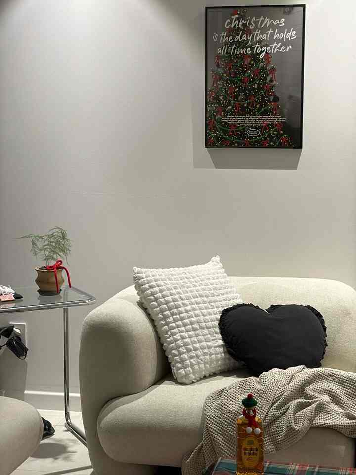 Beige and white toned living room featuring a cozy sofa with cushions and a Christmas tree poster creating a warm atmosphere