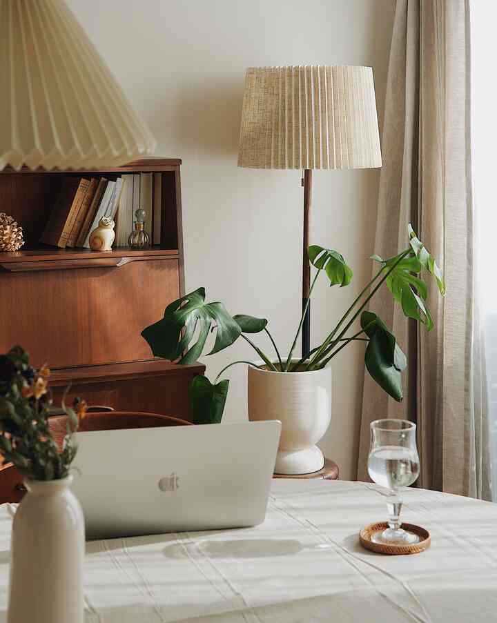 ナチュラルカラーのダイニングルーム、木製のダイニングテーブルと椅子、大きな観葉植物とフロアランプが配された落ち着いた雰囲気のワークスペース