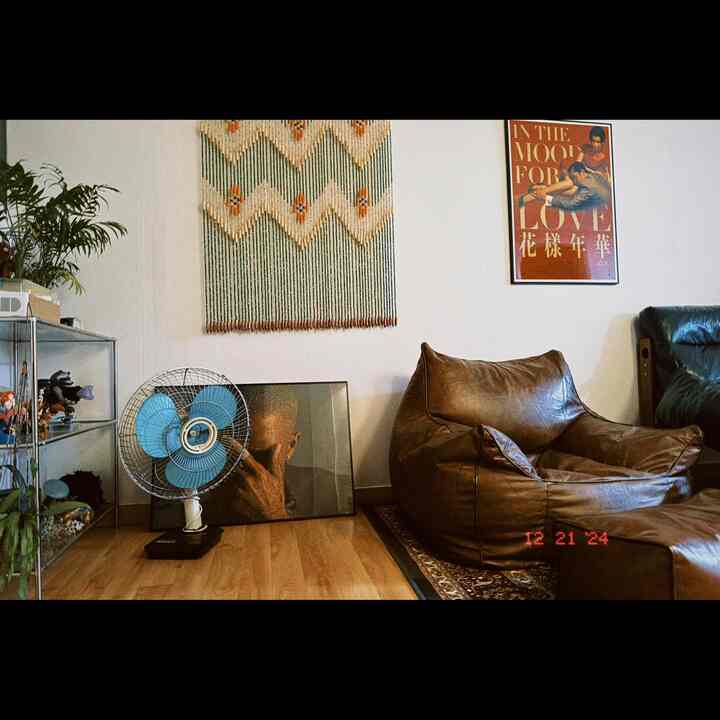 温かみのある木目調の床と白い壁、ヴィンテージスタイルの茶色のビーズクッションと青いレトロな卓上扇風機が配置されたリビング空間