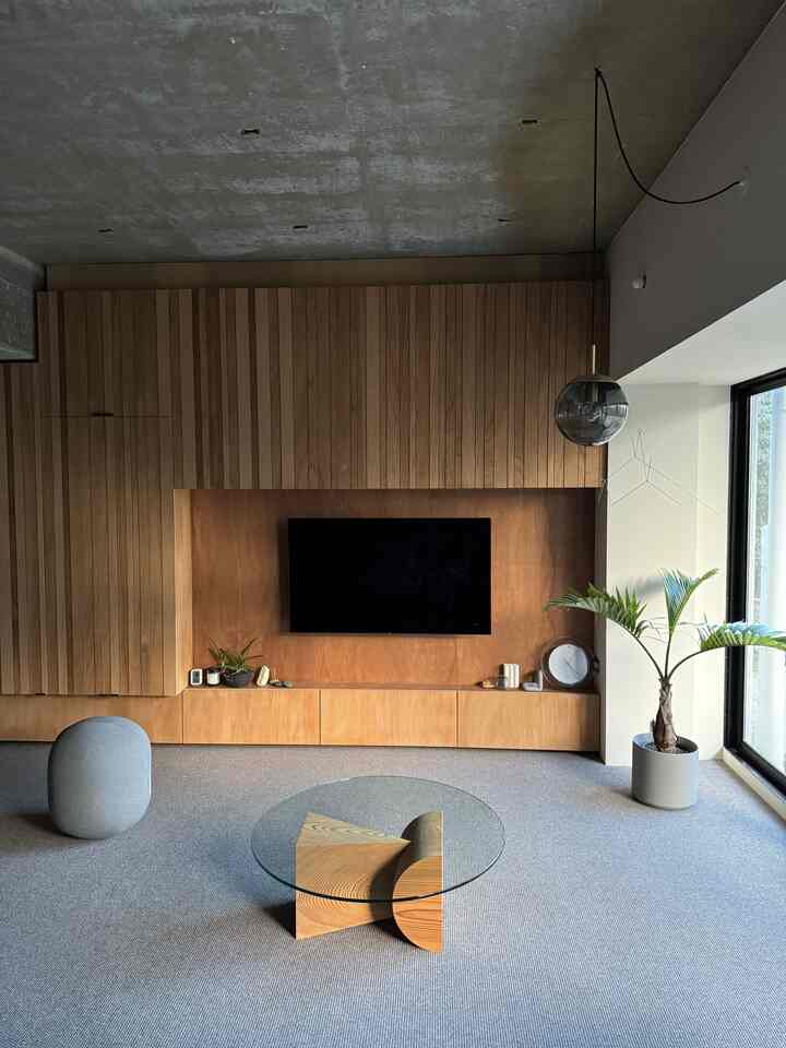ナチュラルトーンのワンルームリビング、木製壁面とカーペット、ペンダントライトが配されたシンプルな空間