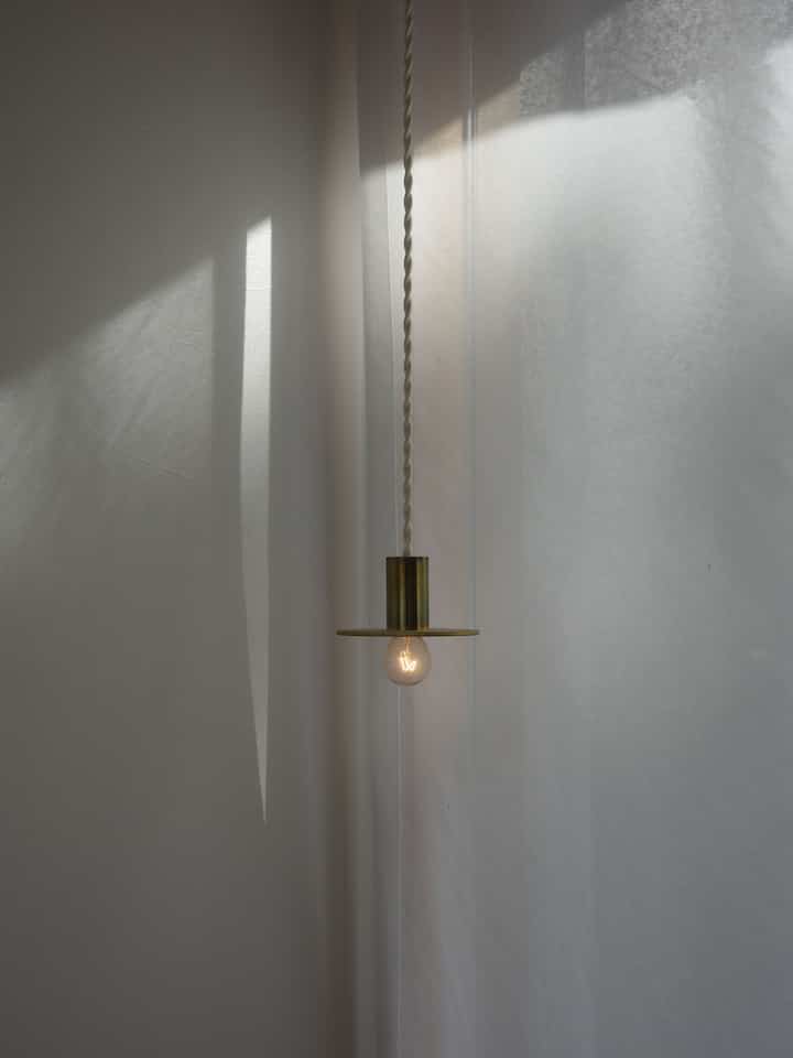 明るい白色調の玄関空間、中央にペンダントライトと薄いカーテンが配置され、シンプルでナチュラルな雰囲気のインテリア