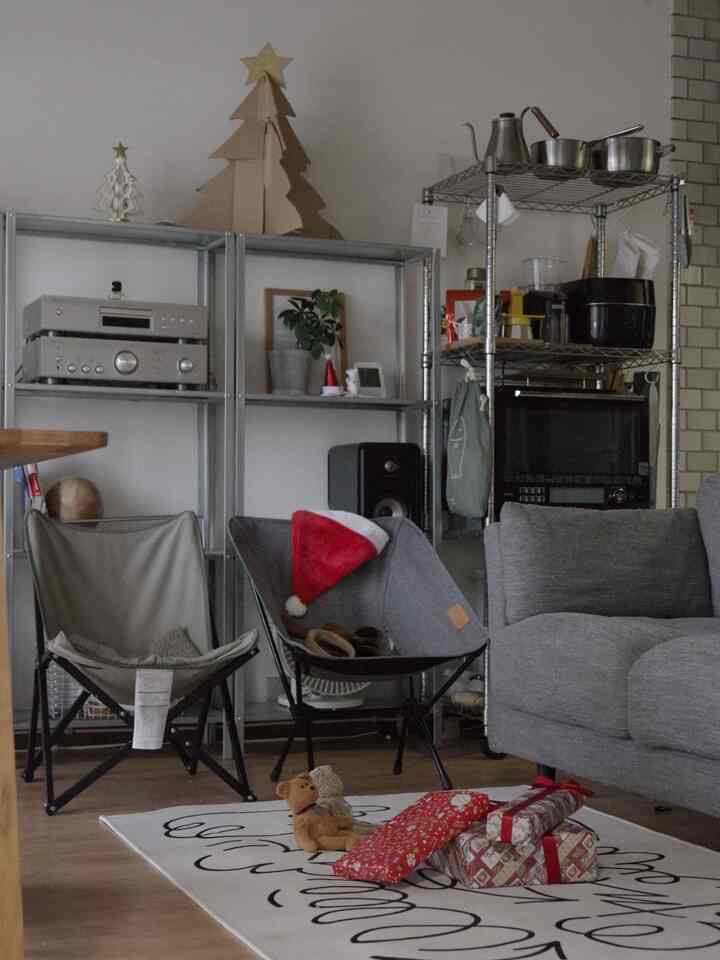 ナチュラルな木目調とグレーのリビング、メタル棚やアームチェア、ラグとギフトが配置された落ち着いた雰囲気のインテリア