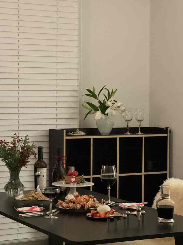 ブラックとホワイトの色調のダイニング、中央に黒いダイニングテーブルと花瓶、ワイングラスが配置された温かみのあるホームパーティースペース