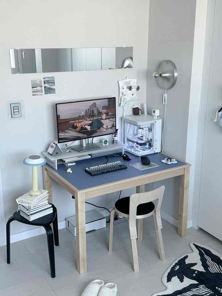 白い壁と青いテーブルトップが際立つホームオフィス、モニターとコンピューター、シンプルな木製デスクとチェアが配置されたミニマルな空間