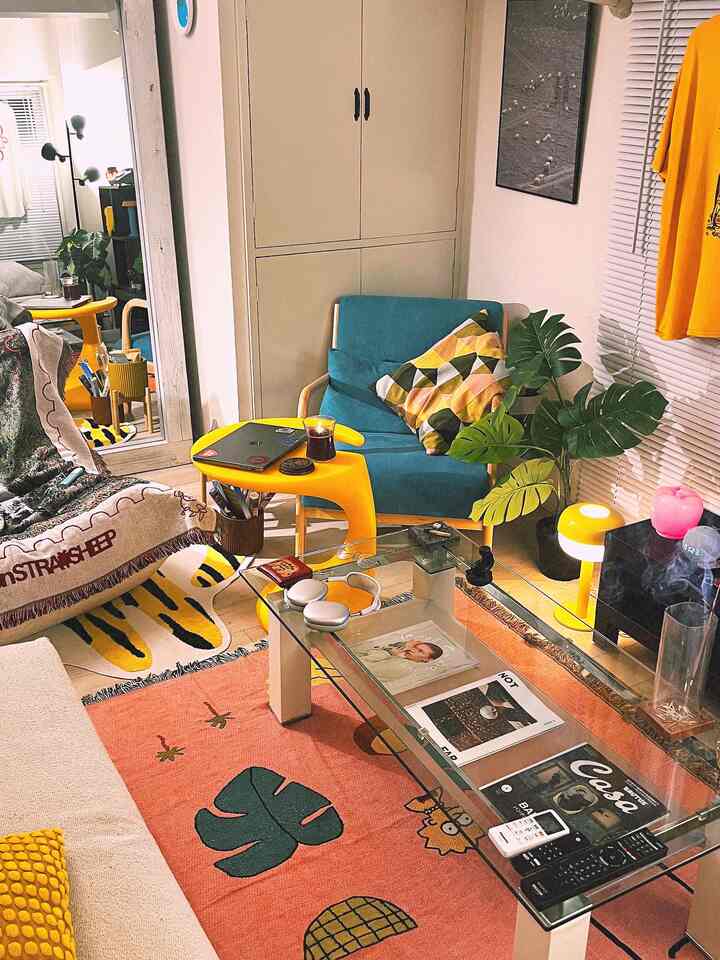 Small living room with yellow and blue sofa and armchair, featuring a glass table and plants creating a cozy atmosphere