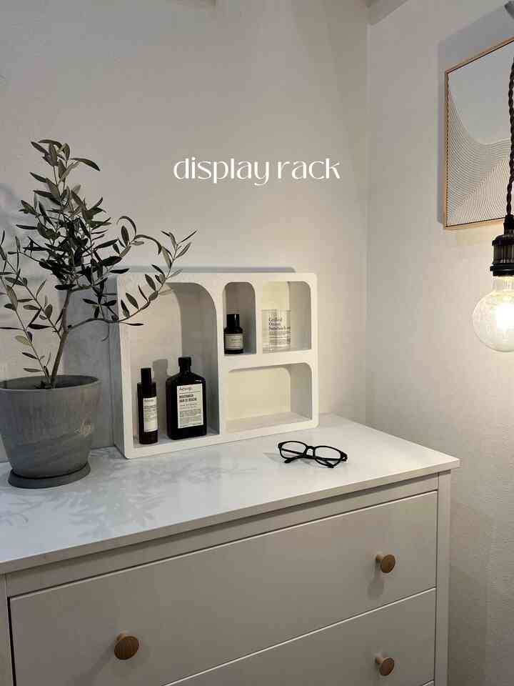 白を基調としたリビングスペース、白いチェストの上にディスプレイラックと化粧品、眼鏡が配され、ミニマルな雰囲気のあるインテリア
