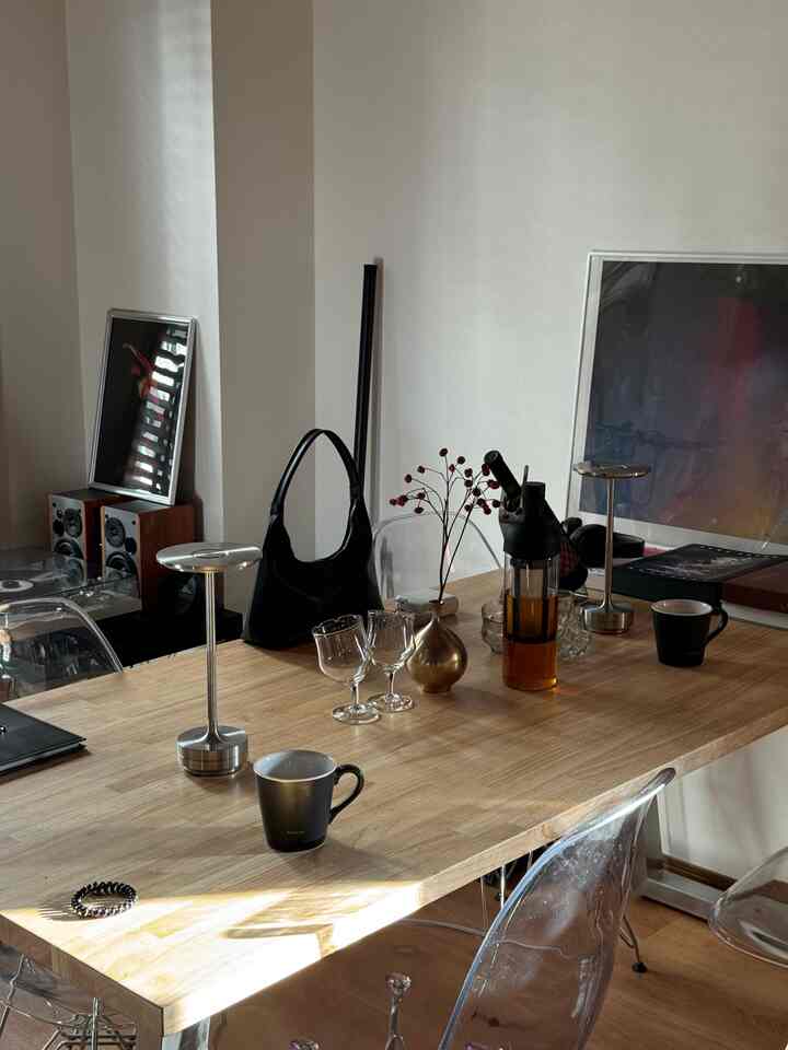 ナチュラルな木目調とシンプルモダンスタイルの1LDKダイニングルーム、大きな木製テーブルと透明な椅子が中央に配置され、テーブルランプや小物が置かれている印象的な空間