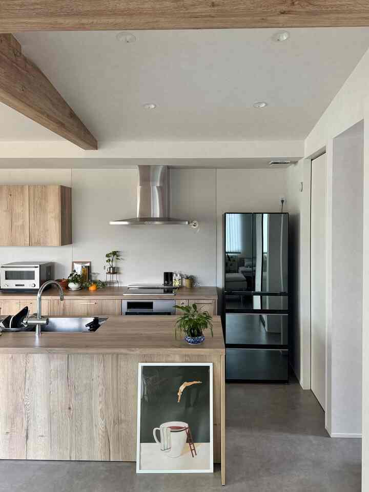 明るい木目調とモダンなデザインのキッチン、中央にキッチンアイランドと黒い家電が配置された印象的な空間