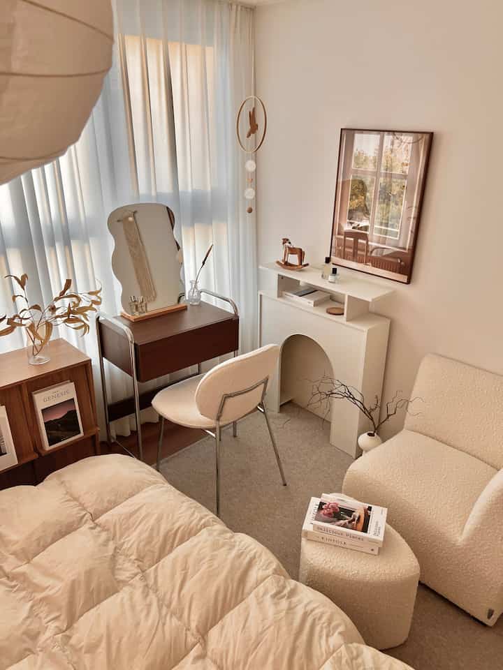 ベージュトーンのワンルーム寝室、ブークレのアームチェアと化粧台が配置された自然な雰囲気のインテリア