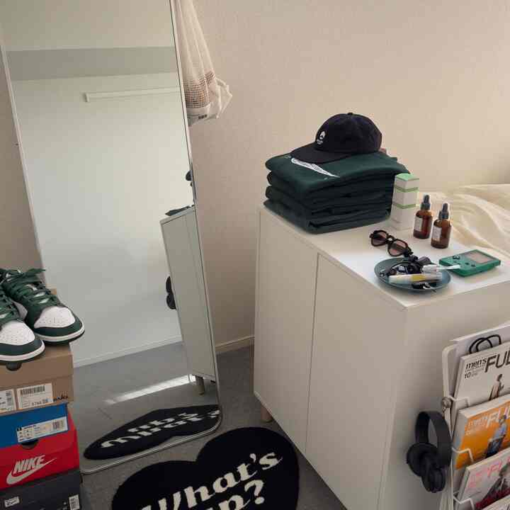 白い壁とキャビネットが特徴のコンパクトなワンルーム、黒いラグと大型の鏡、整然とした空間