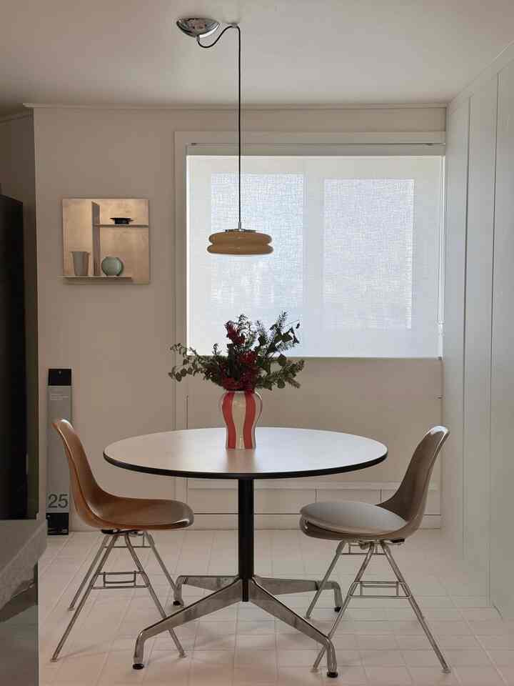 ホワイトとベージュのトーンでまとめられたミッドセンチュリーモダンのダイニングルーム、丸いダイニングテーブルと椅子、ペンダントライトが配置された印象的な空間