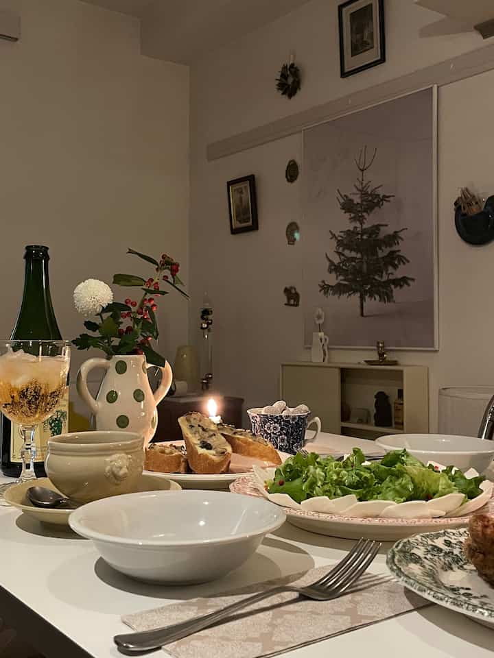 温かみのあるトーンの1Kワンルームのダイニング、白いダイニングテーブルにキャンドルや食器、サラダとクリスマスの飾りが配された雰囲気のあるホームパーティースペース