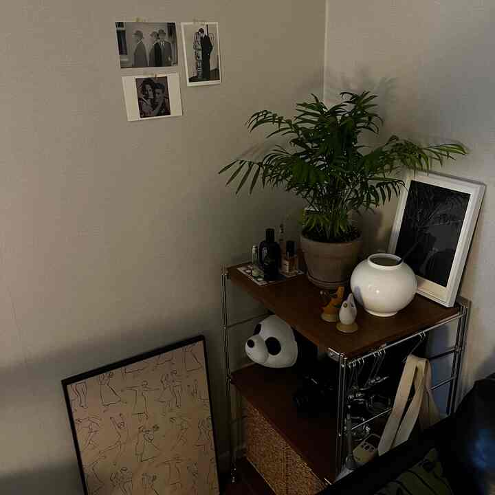 グレーの壁に囲まれたコーナーのリビングスペース、ブラウンの木製棚の上に植物と額縁が配置されたナチュラルでシンプルなインテリア