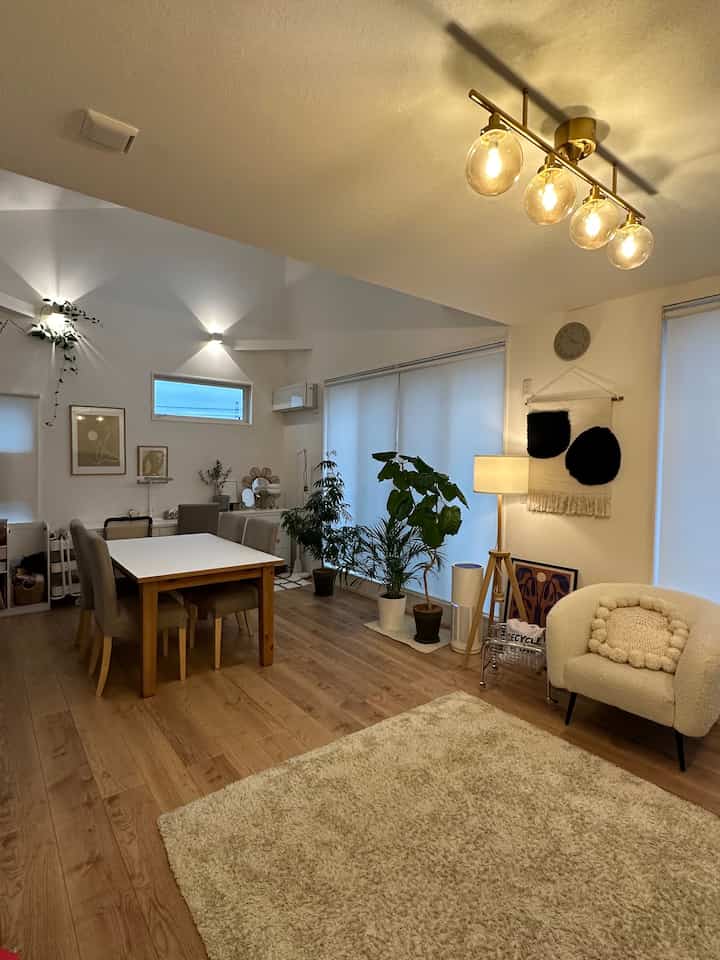 A white and light brown toned Nordic living room featuring a dining table, plants, and floor lamp creating a cozy atmosphere