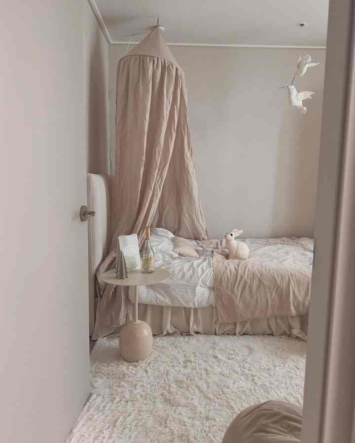 ベージュと白を基調とした小さな子供部屋、キャノピー付きベッドとウサギ形のライトが配された暖かい雰囲気のインテリア