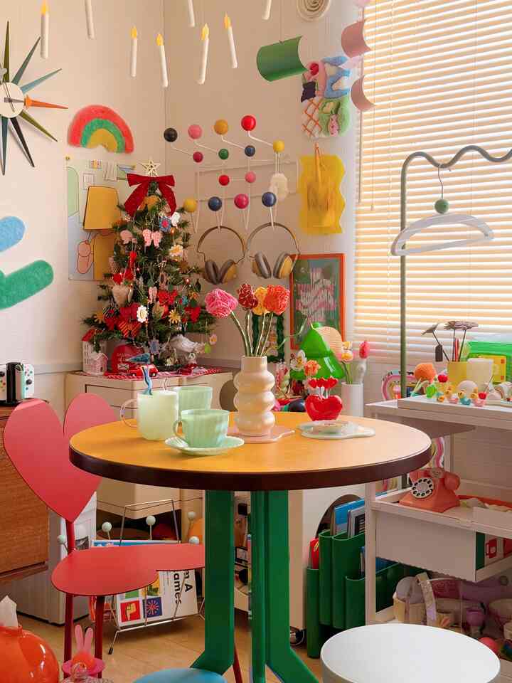 黄色いテーブルと赤いハート型の椅子があるレトロスタイルのリビング、飾り付けられたクリスマスツリーとカラフルな小物が印象的な空間