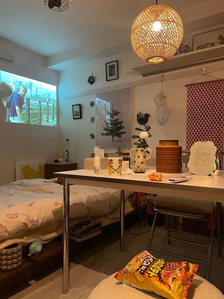 ナチュラルな色調の1Kスタジオリビング、ベッドとテーブルランプ、ポスターが配置された雰囲気のある空間