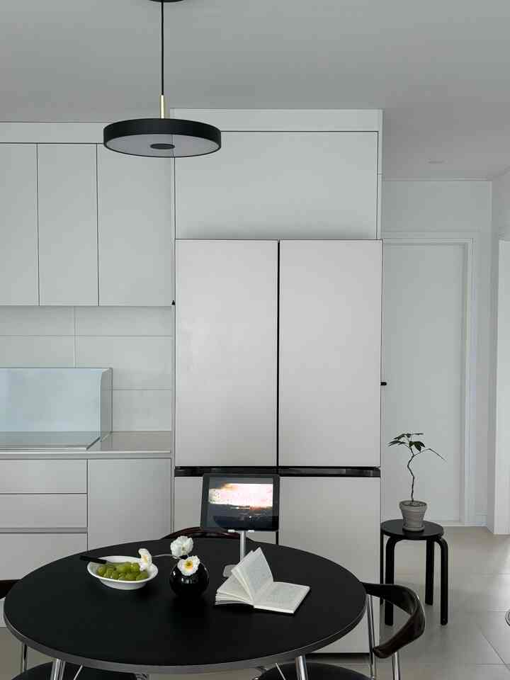 Simple modern dining room in white and black tones featuring a central round dining table with a vase, creating a clean atmosphere