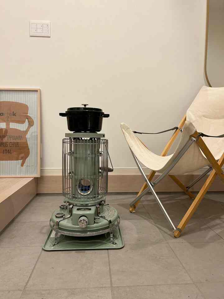 ナチュラルカラーの玄関、ヴィンテージグリーンのストーブとキャンプチェア、額縁が配置された温かみのある雰囲気のインテリア