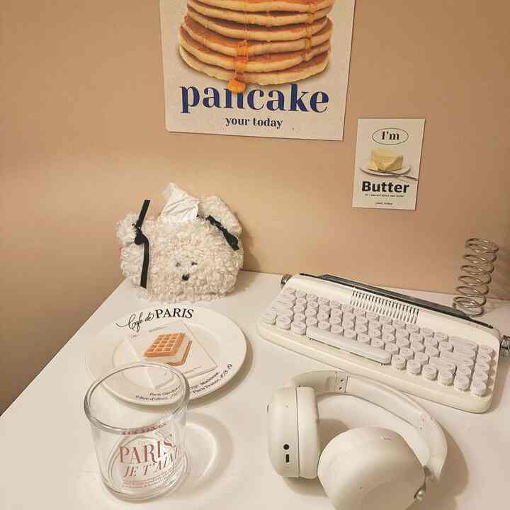 Beige walled Korean interior home office featuring white desk, vintage-style art posters, and white headphones