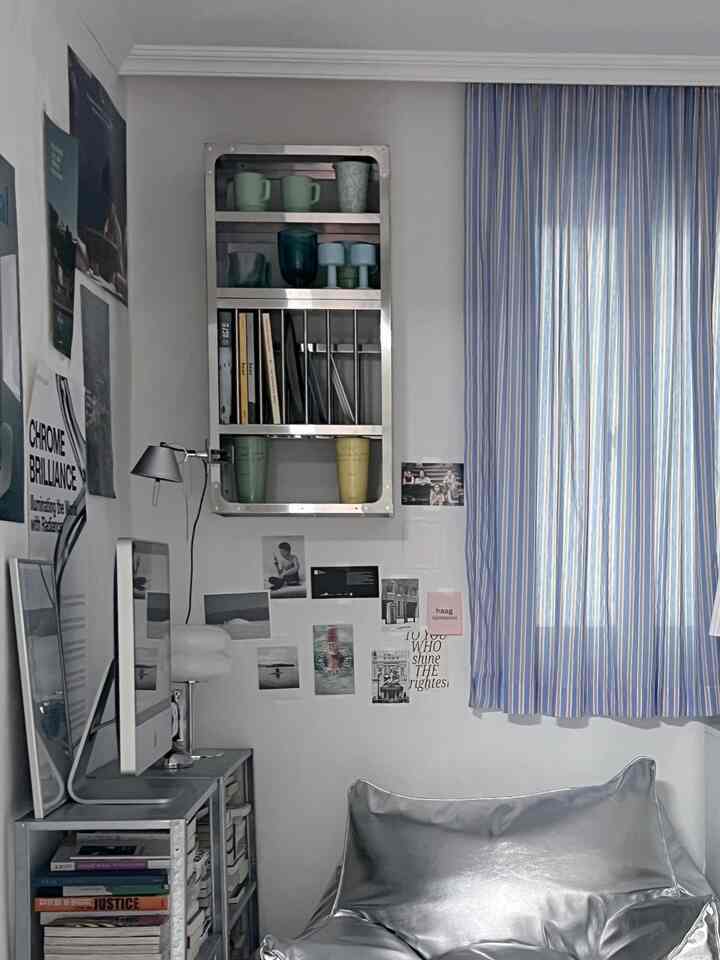 ブルーストライプのカーテンとシルバーのビーズクッションがあるモダンな一人暮らし用の狭い部屋、デスクと収納棚が配置された作業スペース
