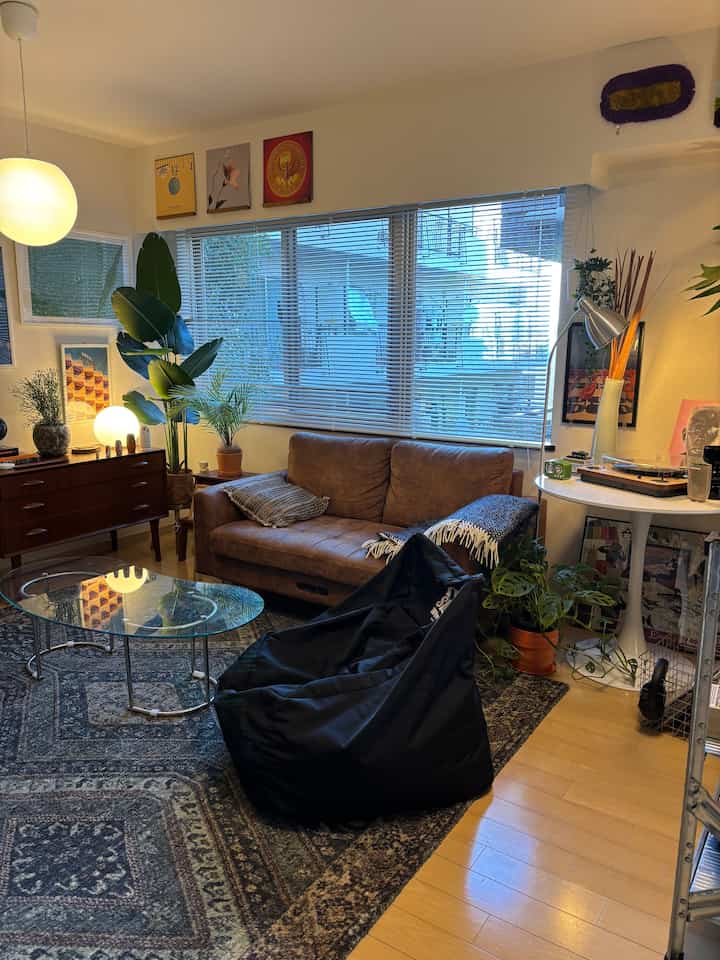 Warm brown natural-toned living room featuring leather sofa, bean bag, plants, and cozy ambiance