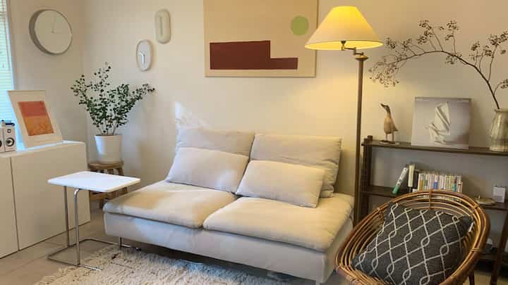 白とベージュのトーンが特徴の1LDKリビング、快適なソファとラタンチェアが配置された自然で落ち着いた雰囲気のインテリア