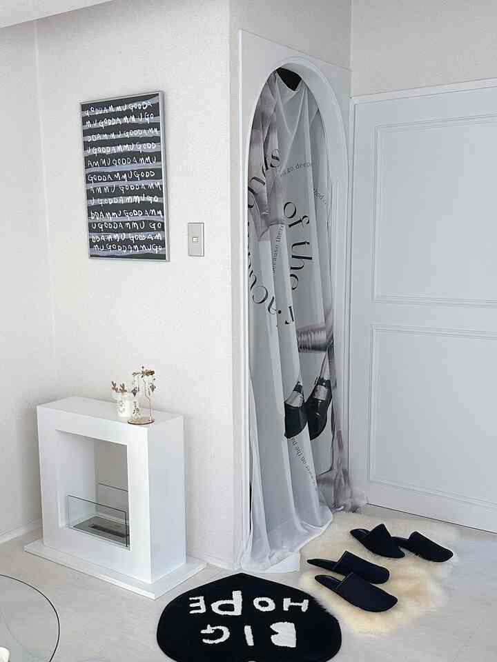 Monotone white entrance space featuring an archway with printed curtain and three pairs of slippers, showcasing a clean minimalist interior