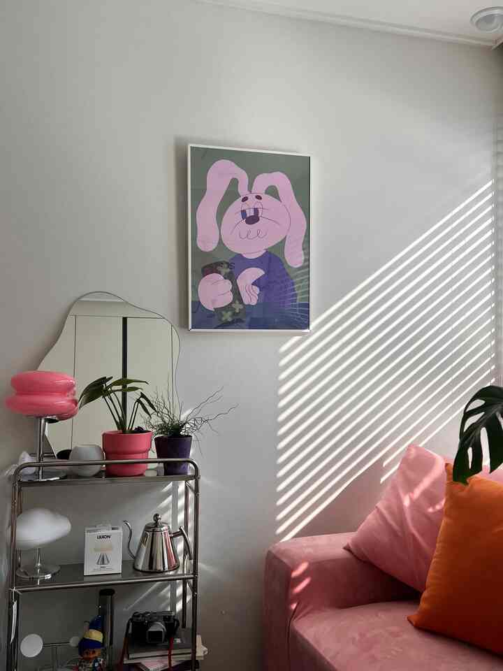 Pink and white toned living room featuring a pink sofa, unique mirror shelf, and plants with a cozy atmosphere