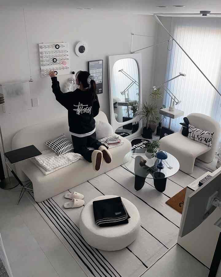 白と黒の色調が特徴のリビング、ホワイトのソファとアームチェア、円形のガラスコーヒーテーブル、大きな鏡と植物が配置されたモダンで落ち着いたインテリア